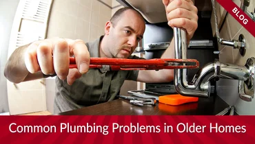 A plumber fixing under-sink pipes with a wrench.